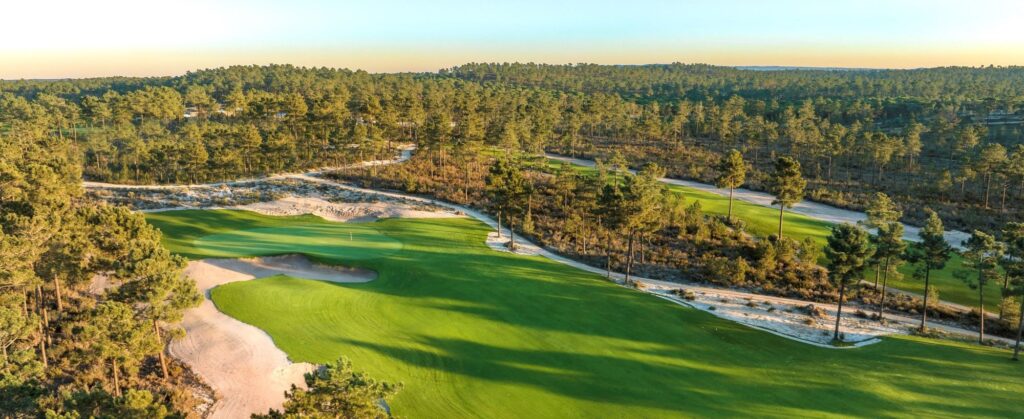 Green playing surfaces framed by dry sandy vegetation at a golf course.