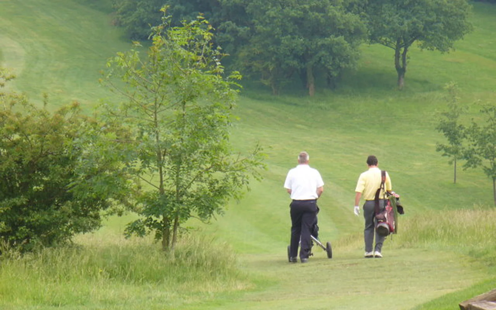 Two golfers walking from the tee with push trolleys at Guildford Golf Club.